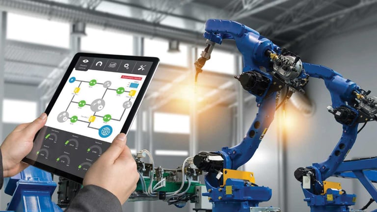 Person holding a tablet displaying a factory automation interface while monitoring two blue industrial robotic arms operating in a modern manufacturing facility.
